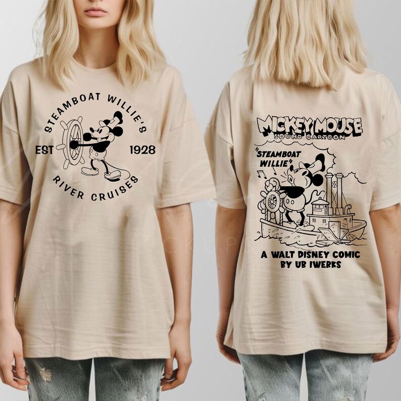 May include: Two beige t-shirts featuring a black and white graphic print of Mickey Mouse on a steamboat. The front of the shirt reads "Steamboat Willie's Est 1928 River Cruises". The back of the shirt reads "Mickey Mouse Sound Cartoon Steamboat Willie A Walt Disney Comic by Ub Iwerks".
