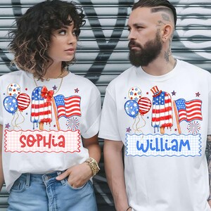 May include: White t-shirts with patriotic designs. One shirt features the name "Sophia" and the other "William". Each shirt has a popsicle design with the American flag, balloons, and fireworks. Ideal for celebrating the 4th of July.