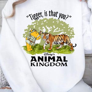 Puede incluir: Sudadera blanca con una imagen de dibujos animados de Winnie de Pooh mirando a un tigre a trav&eacute;s de una lupa. El texto "Tigger, is that you?" est&aacute; por encima de la imagen. Debajo de la imagen est&aacute; el texto "Disney's Animal Kingdom".