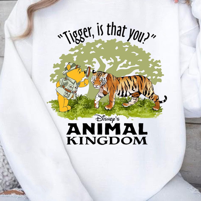 Puede incluir: Sudadera blanca con una imagen de dibujos animados de Winnie de Pooh mirando a un tigre a trav&eacute;s de una lupa. El texto "Tigger, is that you?" est&aacute; por encima de la imagen. Debajo de la imagen est&aacute; el texto "Disney's Animal Kingdom".