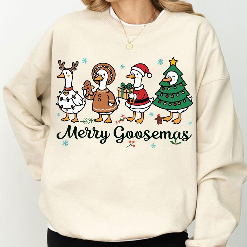 Peut inclure: Un sweat-shirt cr&egrave;me avec un motif festif. Quatre oies de dessin anim&eacute; sont habill&eacute;es pour les f&ecirc;tes. L'une porte des bois de renne, une autre tient un bonhomme en pain d'&eacute;pices, et une autre est habill&eacute;e en P&egrave;re No&euml;l. Le texte "Merry Goosmas" est imprim&eacute; en dessous.