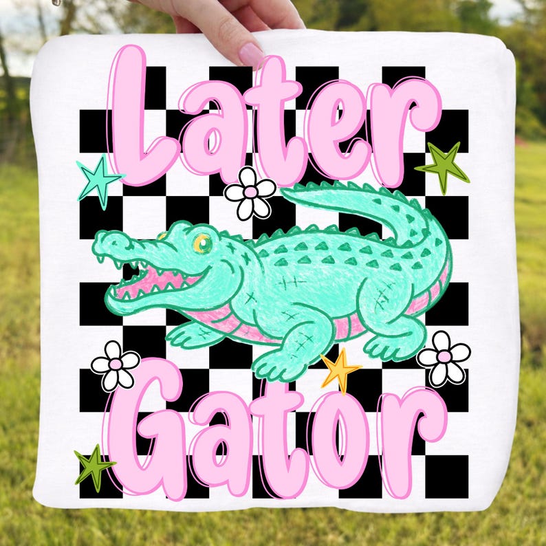 May include: White square towel with a cartoon alligator design. The alligator is teal with pink accents, set against a black and white checkered background. The words "Later Gator" are in pink script.