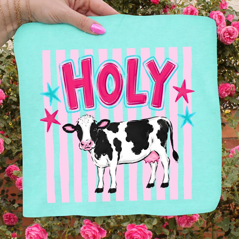 Puede incluir: Un textil cuadrado azul claro con la palabra "HOLY" en letras rosas, delineadas en blanco. Una vaca en blanco y negro est&aacute; debajo del texto, con estrellas rosas y azules y rayas verticales rosas en el fondo.