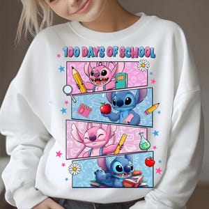 May include: White sweatshirt with a colourful graphic featuring the text "100 Days of School" and cartoon characters. The design includes pink and blue panels with school-themed illustrations like pencils and books.