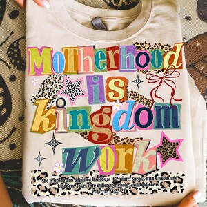 Pu&ograve; includere: Maglietta beige con la scritta multicolore "Motherhood is Kingdom Work". Il design include stelle, fiori e motivi leopardati. Una citazione di Proverbi 31:25-27 &egrave; stampata in basso.