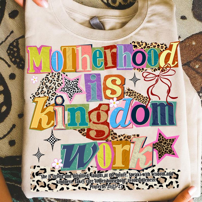 Pu&ograve; includere: Maglietta beige con la scritta multicolore "Motherhood is Kingdom Work". Il design include stelle, fiori e motivi leopardati. Una citazione di Proverbi 31:25-27 &egrave; stampata in basso.