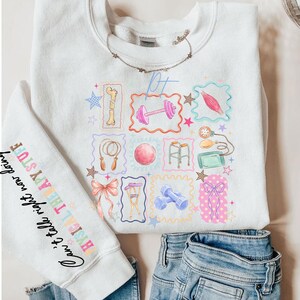 May include: White sweatshirt with a colorful graphic of physical therapy tools and the text "PT". The sleeve features the text "Can't take it right now doing PHYSICAL THERAPY STUFF". The design includes dumbbells, a jump rope, and a pink bow.