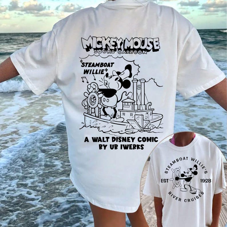 May include: White t-shirt featuring a black and white illustration of Mickey Mouse on a steamboat. The text "Mickey Mouse Sound Cartoon" is above the image and "Steamboat Willie" is below the image. The text "A Walt Disney Comic by Ub Iwerks" is at the bottom of the shirt.