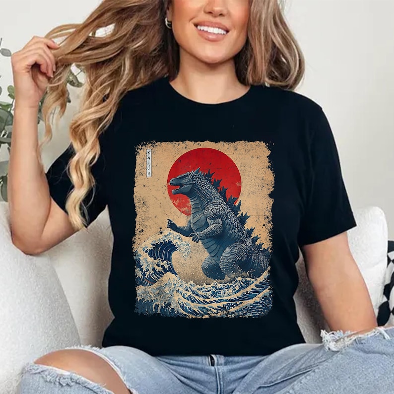 May include: Black t-shirt with a Godzilla-themed design. The graphic shows Godzilla in a traditional Japanese art style, with a red sun and ocean waves. The word "KAIJU" is printed vertically on the left side of the design.