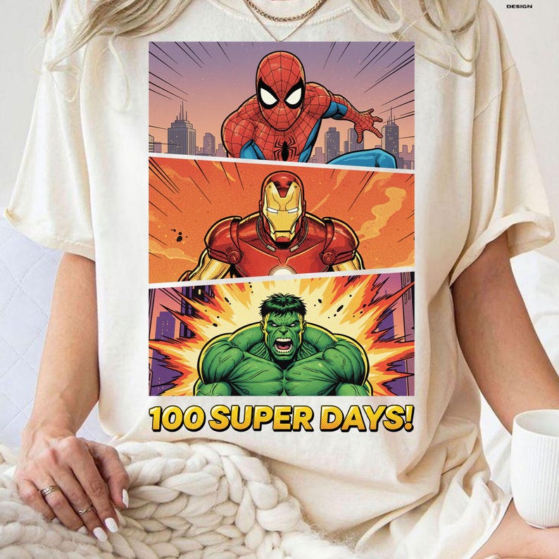 May include: Cream-colored t-shirt featuring a comic book-style graphic of Spider-Man, Iron Man, and the Hulk. The graphic is divided into three panels with a cityscape background. Text at the bottom reads "100 SUPER DAYS!"