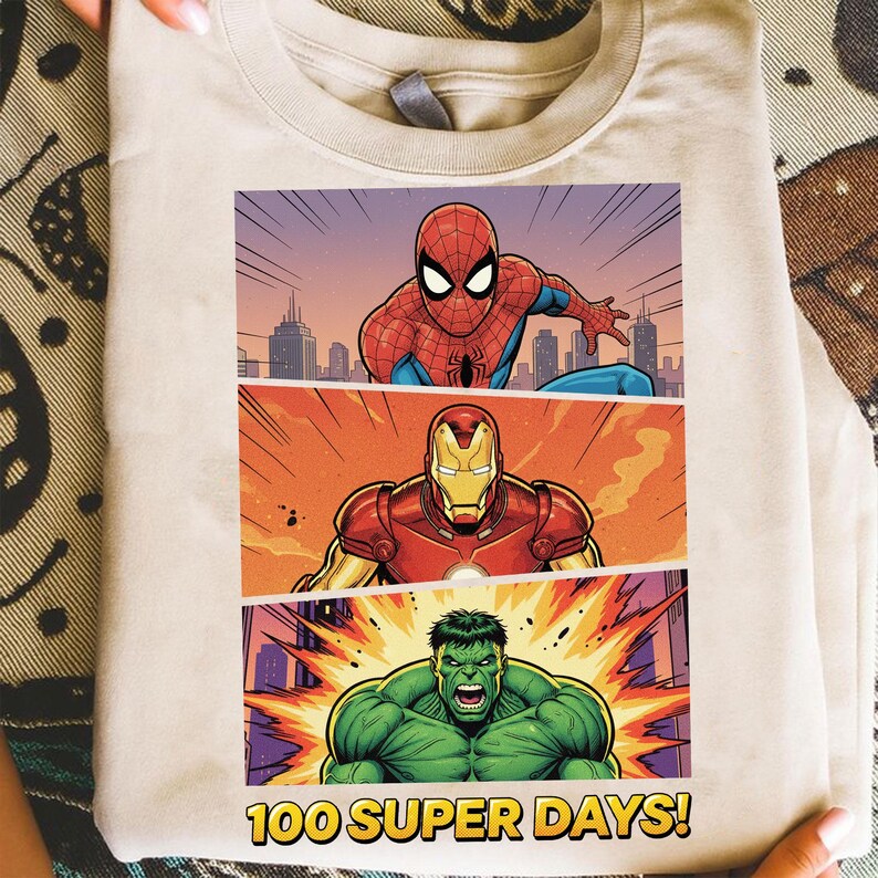 May include: A beige t-shirt featuring a comic book-style graphic of Spider-Man, Iron Man, and the Hulk. The graphic is divided into three panels with a cityscape background. The text "100 SUPER DAYS!" is at the bottom.