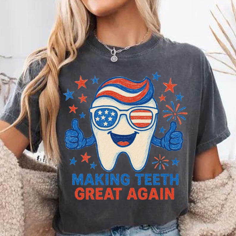 May include: Dark gray t-shirt with a patriotic tooth graphic. The tooth wears sunglasses with an American flag design and gives two thumbs up. The text "MAKING TEETH GREAT AGAIN" is printed below the tooth, surrounded by stars and fireworks.