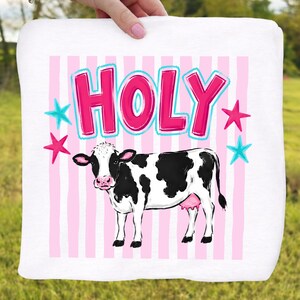 Puede incluir: Toalla blanca con una ilustraci&oacute;n de vaca de dibujos animados. La vaca es blanca y negra con una ubre rosa. La palabra "HOLY" est&aacute; escrita en letras rosas con un contorno azul, y hay estrellas rosas y azules.