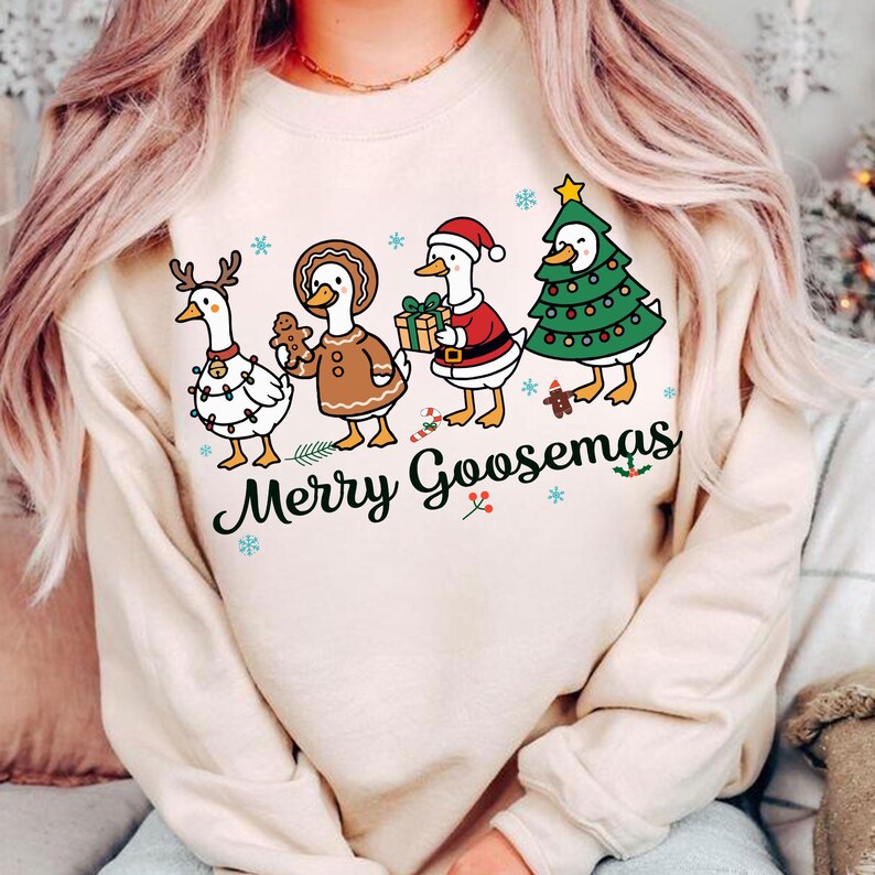 Peut inclure: Un sweat-shirt beige avec un motif de No&euml;l. Il pr&eacute;sente quatre oies habill&eacute;es pour les f&ecirc;tes : une avec des bois et des lumi&egrave;res, une en pain d'&eacute;pices, une en P&egrave;re No&euml;l et une en sapin de No&euml;l. Le texte "Merry Goosemas" est en dessous.