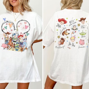 May include: White t-shirt with a front graphic of Disney's Toy Story characters inside a Mickey Mouse outline. The back of the shirt features character names and images, including Buzz Lightyear and Woody.