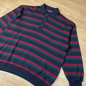 May include: A long-sleeve polo shirt featuring horizontal stripes in navy blue, dark green, and red. The shirt has a classic collar, a three-button placket, and ribbed cuffs at the sleeves and hem. The fabric has a textured knit appearance.