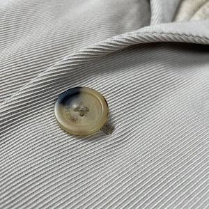 May include: Close-up of a beige button on a beige fabric. The button is round with a light brown and dark brown color scheme. The fabric has a ribbed texture.