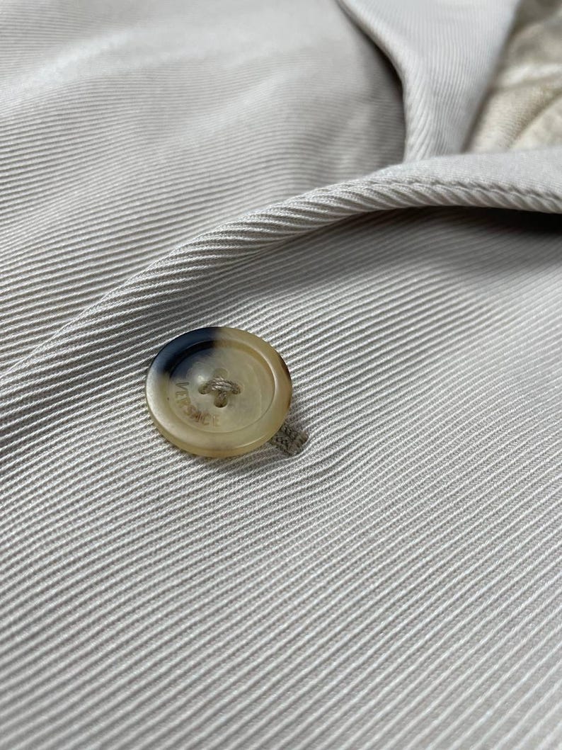 May include: Close-up of a beige button on a beige fabric. The button is round with a light brown and dark brown color scheme. The fabric has a ribbed texture.