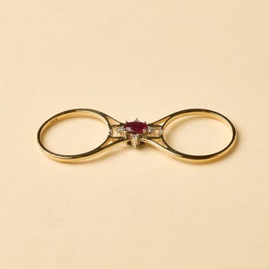 May include: A gold double ring with a red ruby and clear diamonds in the center.