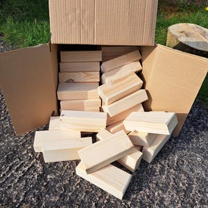 May include: A cardboard box overflowing with natural wood blocks. The blocks are stacked and scattered, showing their smooth, unfinished surface.