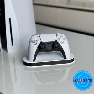 May include: A white and black video game controller on a white charging stand. The controller has a PlayStation logo on the front.