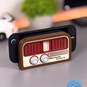 May include: A brown and cream-coloured Nintendo Switch case designed to resemble a vintage radio. The case has a red mesh speaker area, two white knobs, and the words "Nintendo Switch" printed on the front. The Switch console is inserted into the case.