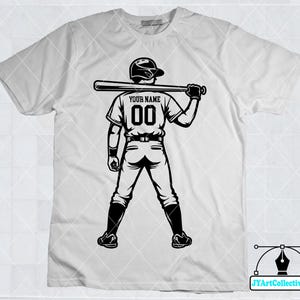 May include: White t-shirt with a black and white illustration of a baseball player holding a bat. The player is wearing a baseball uniform with the text "YOUR NAME" and the number "00" on the back.