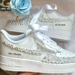 K&ouml;nnte beinhalten: Wei&szlig;e Turnschuhe mit Perlen und Strasssteinen verziert. Die Schuhe haben ein wei&szlig;es Band und die Texte "Mrs. Morales" und "05.19.2026". Die Turnschuhe haben ein klassisches Design mit wei&szlig;er Sohle und dem Wort "AIR" an der Seite.