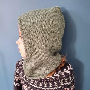 Peut inclure: Un col roulé à capuche en tricot vert avec une texture côtelée. Le col roulé est porté par une personne avec un pull à motifs.