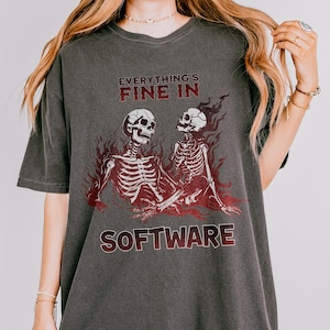 Peut inclure: T-shirt gris foncé avec l'inscription rouge "EVERYTHING'S FINE IN SOFTWARE". Le t-shirt présente un motif de deux squelettes entourés de flammes rouges. Le t-shirt a une coupe ample et des manches courtes.