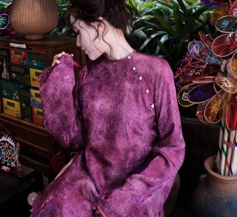 Puede incluir: Vestido magenta de manga larga con estampado floral. El vestido tiene cuello mandar&iacute;n y se abrocha con peque&ntilde;os botones blancos. Las mangas son anchas y fluidas. La tela parece ligera y semitransparente.