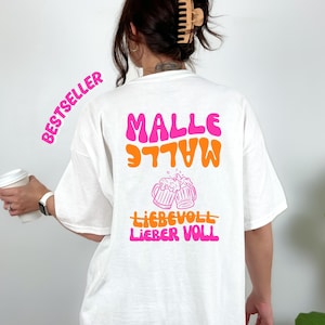 Könnte beinhalten: Weißes T-Shirt mit dem Text "MALLE" in Pink und "LIEBER VOLL" in Orange. Das Shirt zeigt auch eine Grafik von zwei Bierkrügen, die anstoßen. Das Wort "BESTSELLER" ist pink auf der linken Seite gedruckt.