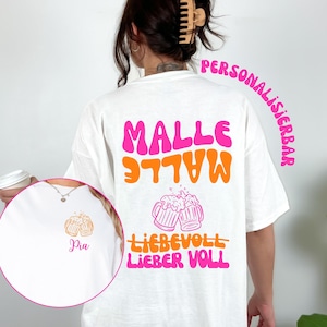 Könnte beinhalten: Weißes T-Shirt mit dem Wort "MALLE" in Pink und Orange sowie "LIEBEVOLL LIEBER VOLL" in Orange und Pink. Das Shirt zeigt auch eine Grafik von zwei Bierkrügen. Das Wort "PERSONALISIERBAR" ist in Pink geschrieben.