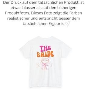May include: White t-shirt with the text "THE BRIDE" in pink and orange retro font. Below the text is a cocktail glass design with a cherry, bow, and star accents. A bridal party theme.