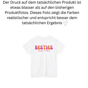 May include: White t-shirt with the word "BESTIES" in orange and pink retro font. Below the word "BESTIES" is the text "Johanna & Hina" in a cursive font. The shirt is a simple, casual style.
