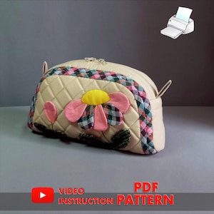 Puede incluir: Una bolsa de maquillaje acolchada beige con una aplicación de flor rosa y ribete de cuadros. La bolsa tiene cierre de cremallera y un asa superior. La imagen incluye el texto "VIDEO INSTRUCTION PATTERN" y "PDF PATTERN".