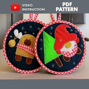 May include: Two round Christmas-themed pot holders. One features a reindeer with a red and white checkered scarf and a gold ornament. The other has a gnome with a red hat and a green Christmas tree. Both have a navy blue background with white stars and a red and white checkered border. The text "VIDEO INSTRUCTION" and "PDF PATTERN" are visible.