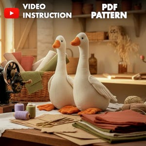 Può includere: Due oche di peluche bianche con becco e zampe arancioni sono esposte su un tavolo di legno. L'immagine include forniture per cucire, tessuto e il testo "VIDEO INSTRUCTION" e "PDF PATTERN". Una macchina da cucire vintage è visibile sullo sfondo.