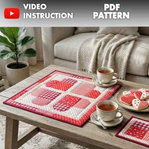 May include: A quilted placemat with a heart pattern in red and white, along with matching coasters and heart-shaped cookies. Two cups of tea sit on the table, with the words "VIDEO INSTRUCTION" and "PDF PATTERN" visible.