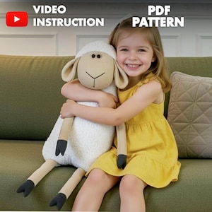 May include: A plush sheep toy with a cream-colored body, tan face, and black hooves is being hugged by a smiling child wearing a yellow dress. The image includes the text "VIDEO INSTRUCTION" and "PDF PATTERN".