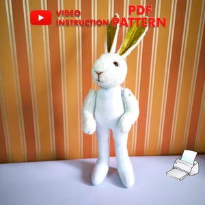 Könnte beinhalten: Ein weißes Plüschkaninchen mit goldenen Ohren steht auf einem gestreiften orange-weißen Hintergrund. Der Text "VIDEO INSTRUCTION PATTERN" und "PDF" ist oben im Bild sichtbar. Ein Drucker-Symbol befindet sich in der unteren rechten Ecke.