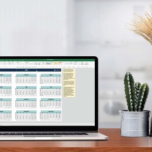 Puede incluir: Un ordenador portátil que muestra una hoja de cálculo con un calendario para cada mes del año. El calendario está en un esquema de colores azul claro y azul oscuro. El portátil está sobre un escritorio de madera con una planta de cactus en una maceta de metal y un ramo de hierba seca en un jarrón de cerámica negra.