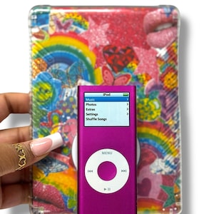 Puede incluir: Un iPod rosa con una funda transparente que presenta un arcoíris y diseños coloridos. La pantalla del iPod muestra las opciones de menú: Música, Fotos, Extras, Ajustes y Reproducción aleatoria.