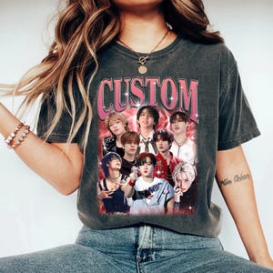 May include: A gray t-shirt with a pink "CUSTOM" graphic featuring a group of men. The graphic has a red and white background with a glittery effect.