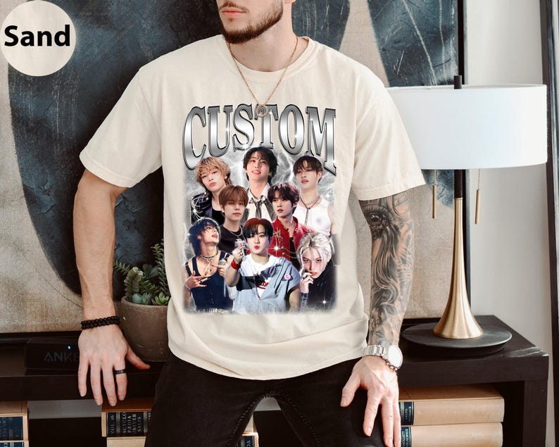 May include: A beige t-shirt with a graphic print of a group of people. The print features the word "CUSTOM" in a silver metallic font. The people in the print are wearing various clothing and have different hairstyles.
