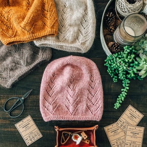 May include: Four knitted hats in different colors and patterns. The hats are made with a soft, textured yarn and have a delicate stitch pattern. The hats are arranged on a wooden surface with other craft supplies.