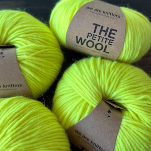 May include: Three skeins of neon yellow yarn, each wrapped with a brown paper label. The labels feature the text "we are knitters" and "THE PETITE WOOL 100% PERUVIAN HIGHLAND WOOL" printed in black ink, along with small care icons.