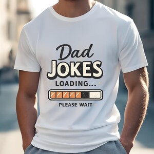 Peut inclure: Un t-shirt blanc à manches courtes avec le texte noir Dad JOKES LOADING... et un graphique représentant une barre de chargement avec des segments orange, suivi du texte PLEASE WAIT, le tout centré sur la poitrine du vêtement.