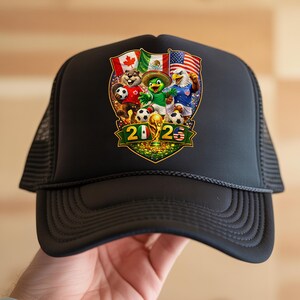 May include: A black trucker hat featuring a graphic of a beaver, a parrot, and an eagle playing soccer with the flags of Canada, Mexico, and the USA. The design includes a gold trophy and the text 2026 with the Mexican and American flags inside the numbers.