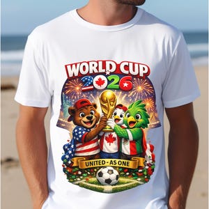 May include: White t-shirt featuring a colorful graphic for the 2026 World Cup. The design includes cartoon mascots holding the World Cup trophy, fireworks, and the text "WORLD CUP 2026" and "UNITED - AS ONE". A soccer ball is at the bottom.